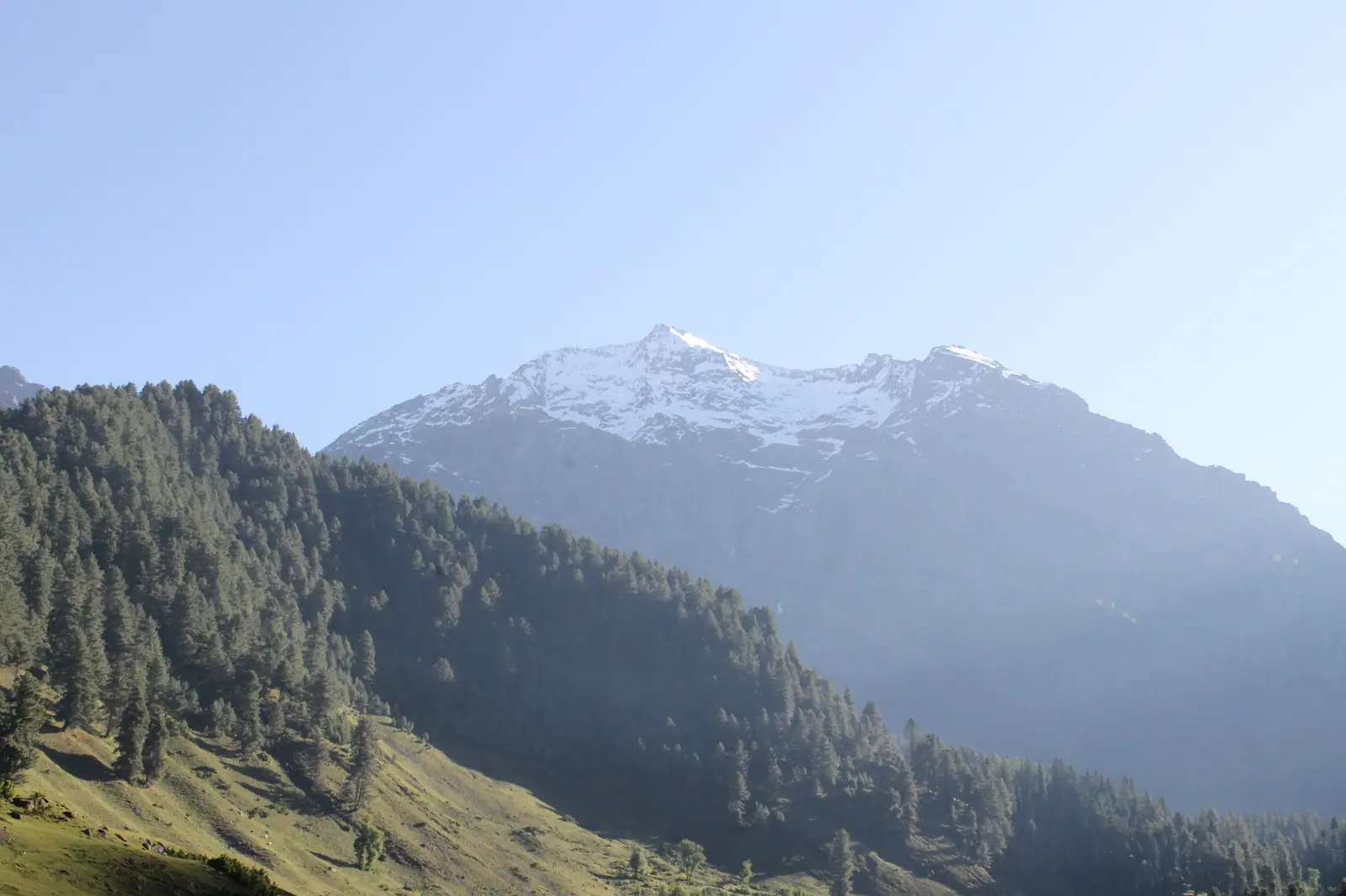 Morning light over forested ridges and a snow peak in Aru Valley