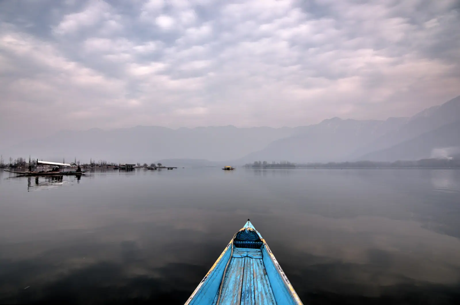 The bow of a shikara pointing across calm Dal Lake